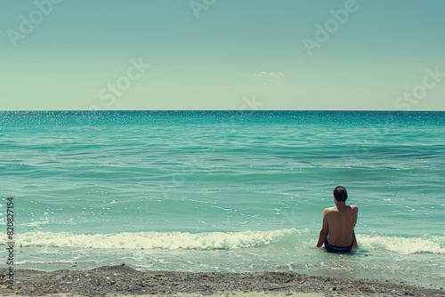 Man sitting alone on the beach gazing at the ocean.