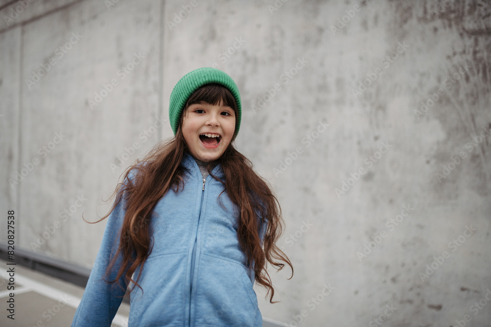 Outdoor portrait of cute young girl with beanie hat. Girl with long hair standing on playground in the city. Outdoor portrait of cute young girl with beanie hat. Girl with long hair standing on playground in the city.