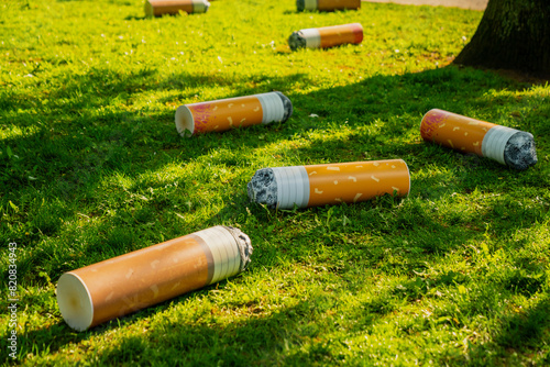 Big plastic cigarettes on the ground as illustration for social issue of tobacco addicition on a green grass background photo