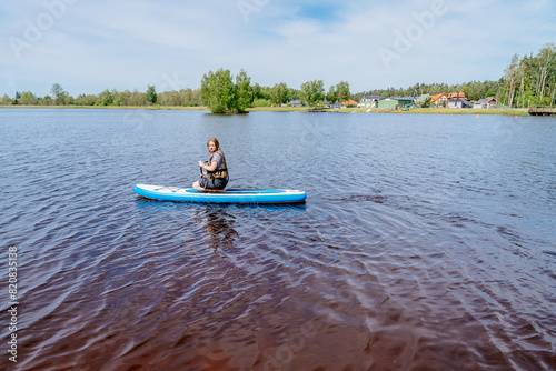 A woman is seated on a paddle board in the center of a lake