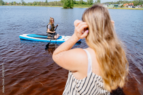 A woman takes a photo of a her friend paddle boarding on water