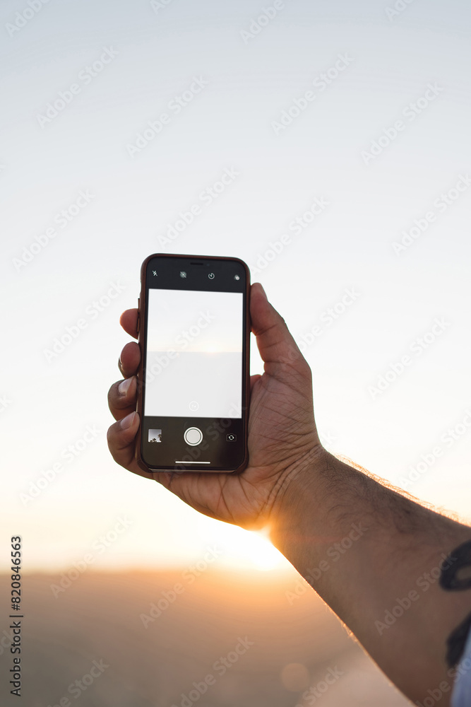 Cropped image of male using smartphone with blank copy space screen on background of beautiful sunset in evening, man's hand holding mobile phone with mock up area for web content or app on display Cropped image of male using smartphone with blank copy space screen on background of beautiful sunset in evening, man's hand holding mobile phone with mock up area for web content or app on display