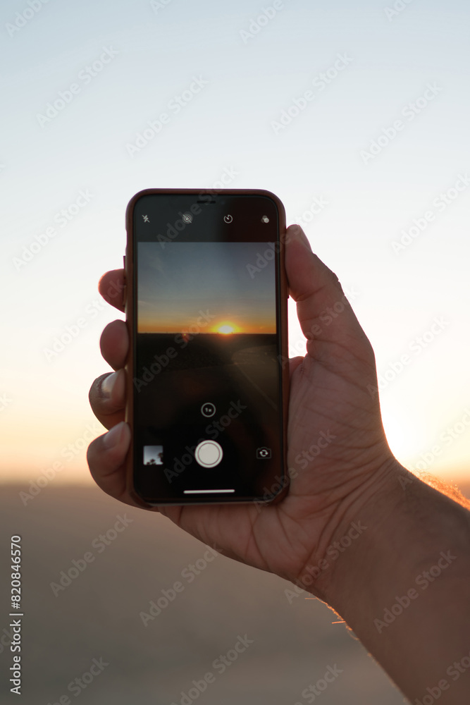 Cropped image of man's hand holding modern smartphone using application for taking evening photos of beautiful sundown, closeup view of male shooting video of sunset and skyline on telephone camera Cropped image of man's hand holding modern smartphone using application for taking evening photos of beautiful sundown, closeup view of male shooting video of sunset and skyline on telephone camera