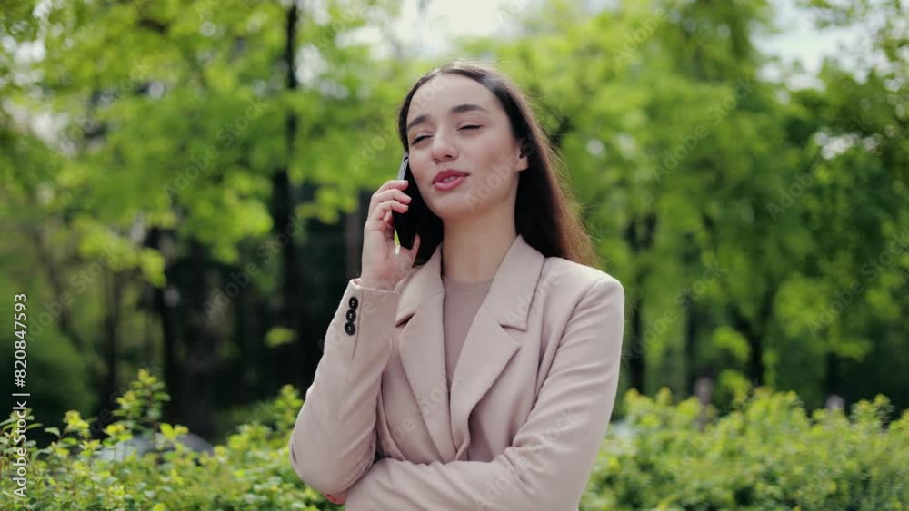 Positive female in stylish outfit talking emotionally by smartphone while standing in public park during daytime. Attractive lady contacting with friends and discussing daily topics and plans. Positive female in stylish outfit talking emotionally by smartphone while standing in public park during daytime. Attractive lady contacting with friends and discussing daily topics and plans.