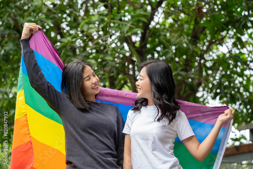 Happy Asian lesbian couple with rainbow flags in the park