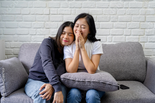 Happy Asian lesbian couple showing love sitting on sofa in home, LGBT pride