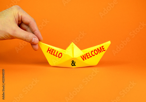 Hello and welcome symbol. Concept words Hello and welcome on beautiful yellow paper boat. Beautiful orange background. Businessman hand. Business hello and welcome concept. Copy space. © Dzmitry