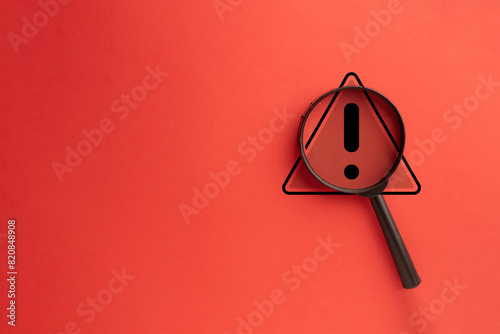 Wall Mural Close-Up View of Warning Triangle Icon Under Magnifying Glass on Red Background: Highlighting Hazard Awareness
