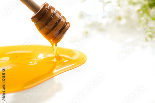 Honey dripping, pouring from wooden honey dipper spoon, isolated on white background. Close-up. Healthy organic liquid honey spill