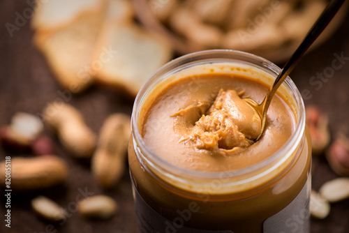 Peanut butter. Creamy smooth peanut butter in jar on a table. Spoon of natural organic vegan food. American cuisine. 