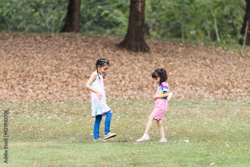 Group of two cute little girls in park. Asian and Caucasian children friends in lawn have fun playing together outdoor in nature, laughing, smiling in casual clothes. Happy, friendship, diversity