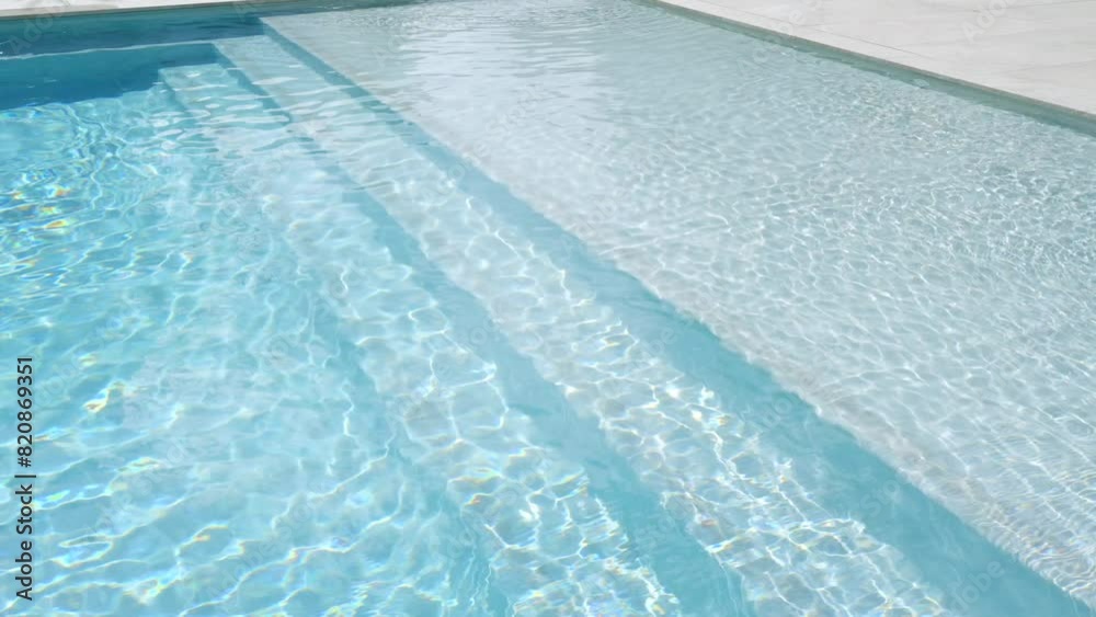 Close up view of swimming pool with clear blue water. Sunlight reflecting sun and creating patterns of light and shadow. Outdoors setting