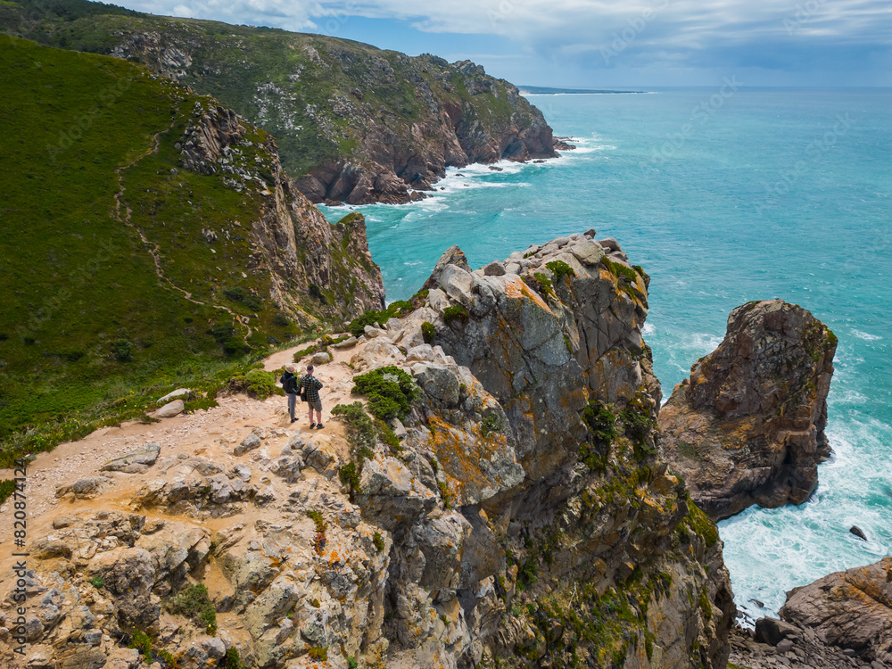 Fototapeta premium Cabo da Roca is the westernmost cape of the Eurasian continent, located in Portugal. A couple stands on a rocky ocean shore.