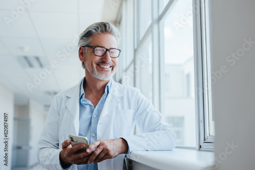 Happy senior doctor holding a mobile phone in a hospital photo