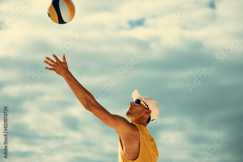 Male athlete spiking yellow volleyball on beach during championship game photo