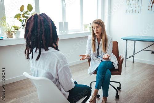 A young female of African ethnicity sits on the examination table at her gynaecologist's office. She is talking to her doctor about her health history. Doctor is checking patient symptom photo