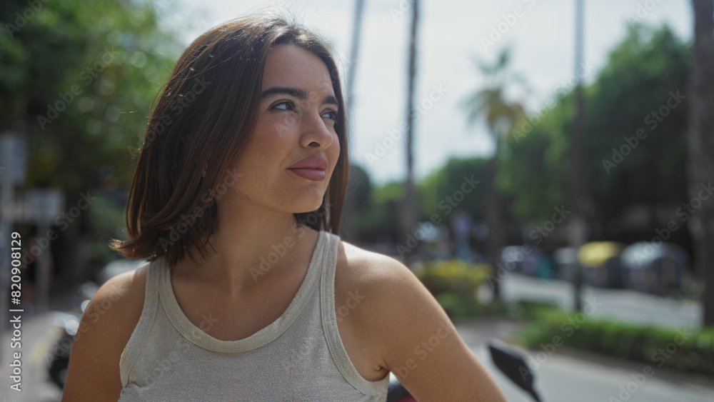Beautiful young hispanic brunette woman standing outdoors on an urban street in a city setting, with trees and traffic in the background, appearing thoughtful and serene. Beautiful young hispanic brunette woman standing outdoors on an urban street in a city setting, with trees and traffic in the background, appearing thoughtful and serene.