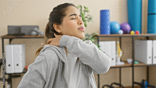 A young hispanic woman experiences neck pain in a rehabilitation clinic s therapy room.