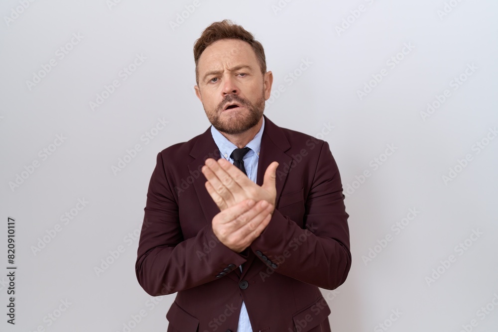 Middle age business man with beard wearing suit and tie suffering pain on hands and fingers, arthritis inflammation Middle age business man with beard wearing suit and tie suffering pain on hands and fingers, arthritis inflammation