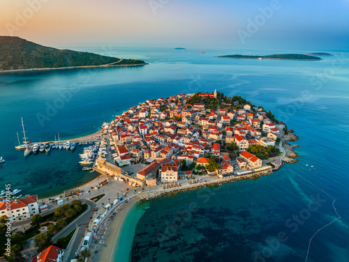 Primosten, Croatia - Aerial view of Primosten peninsula, St. George's Church and old town on a sunny summer morning in Dalmatia, Croatia. Gold and blue sky, yacht marina and turquoise sea water