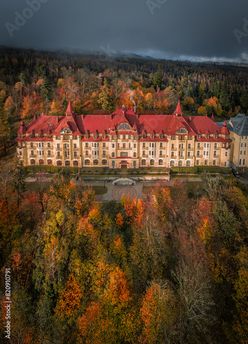 Tatrzanska Lomnica, Slovakia - Aerial view of beautiful warm colorful forest at a hotel by the High Tatras with golden autumn foliage and foggy mountains at background at sunset