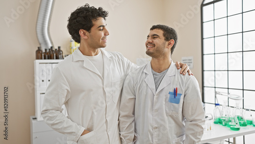 Two men in white lab coats bonding and smiling in a well-equipped modern laboratory.