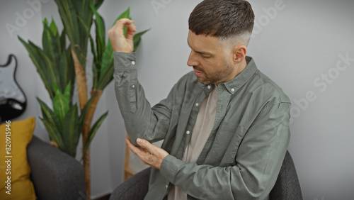 Obraz na plátně Handsome hispanic man with a beard feeling elbow pain in a modern living room interior