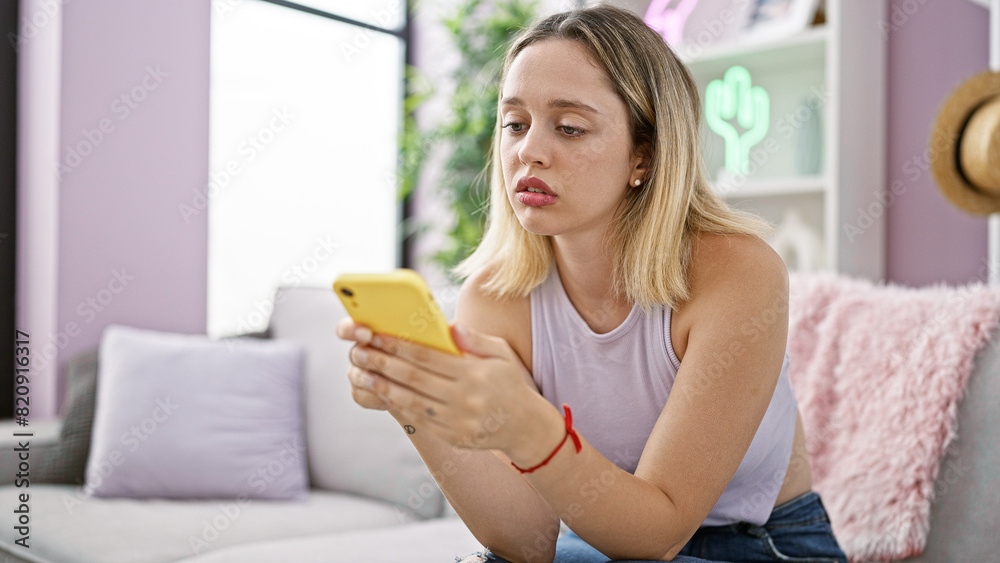 Young blonde woman using smartphone sitting on sofa at home Young blonde woman using smartphone sitting on sofa at home