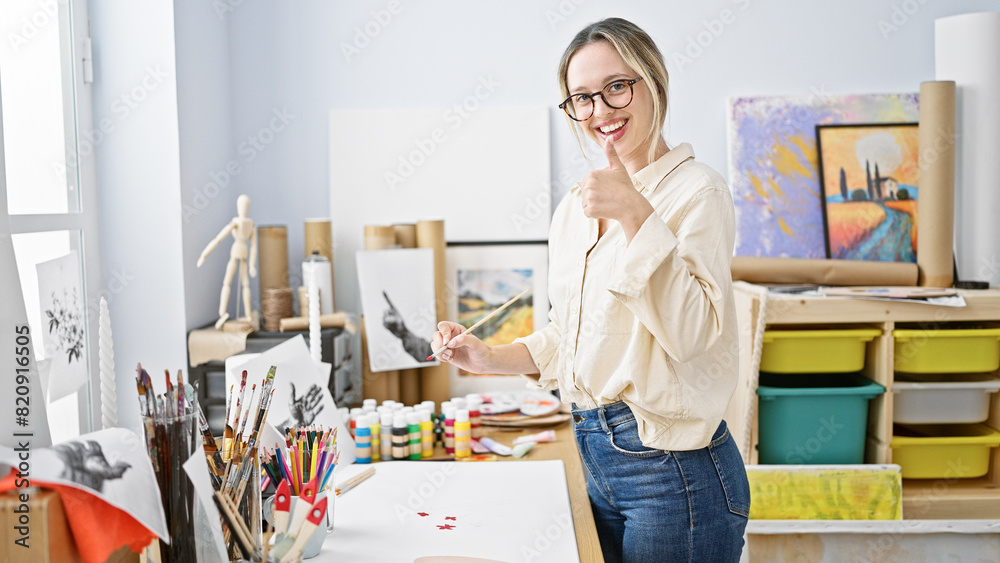 Young blonde woman artist drawing on paper doing thumb up gesture at art studio Young blonde woman artist drawing on paper doing thumb up gesture at art studio