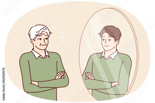 Elderly man stands in front of mirror and sees himself as young guy feeling surge of energy. Young guy looks at grandfather who looks like grandson or son for concept of generational heredity