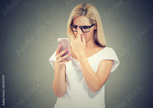Young woman wearing eyeglasses with eyesight problems trying to read phone text 