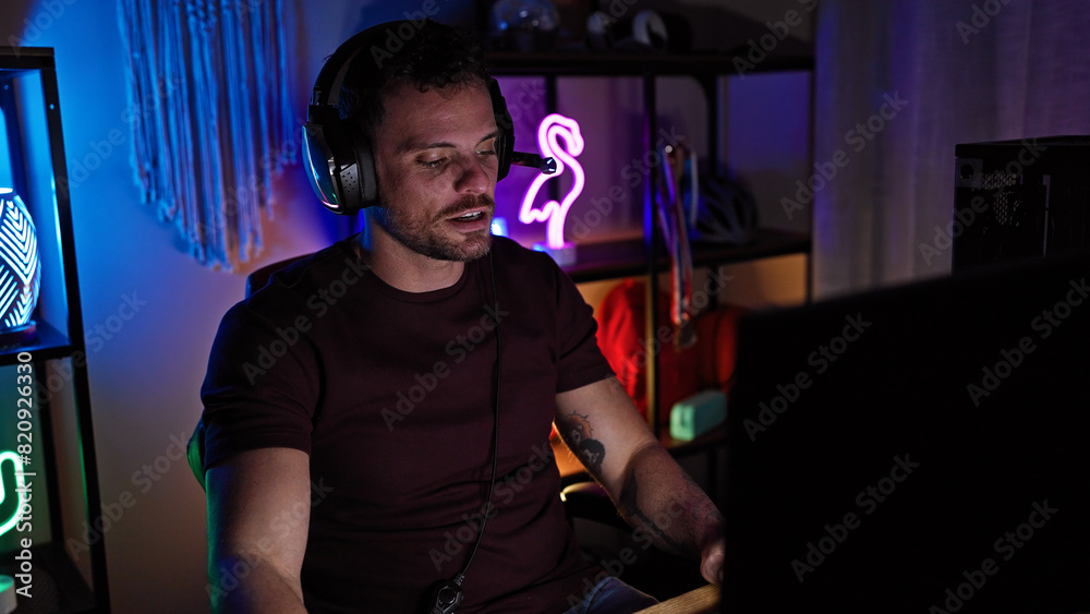 Handsome hispanic man with beard playing video games in a dark gaming room at night, displaying a focused expression. Handsome hispanic man with beard playing video games in a dark gaming room at night, displaying a focused expression.
