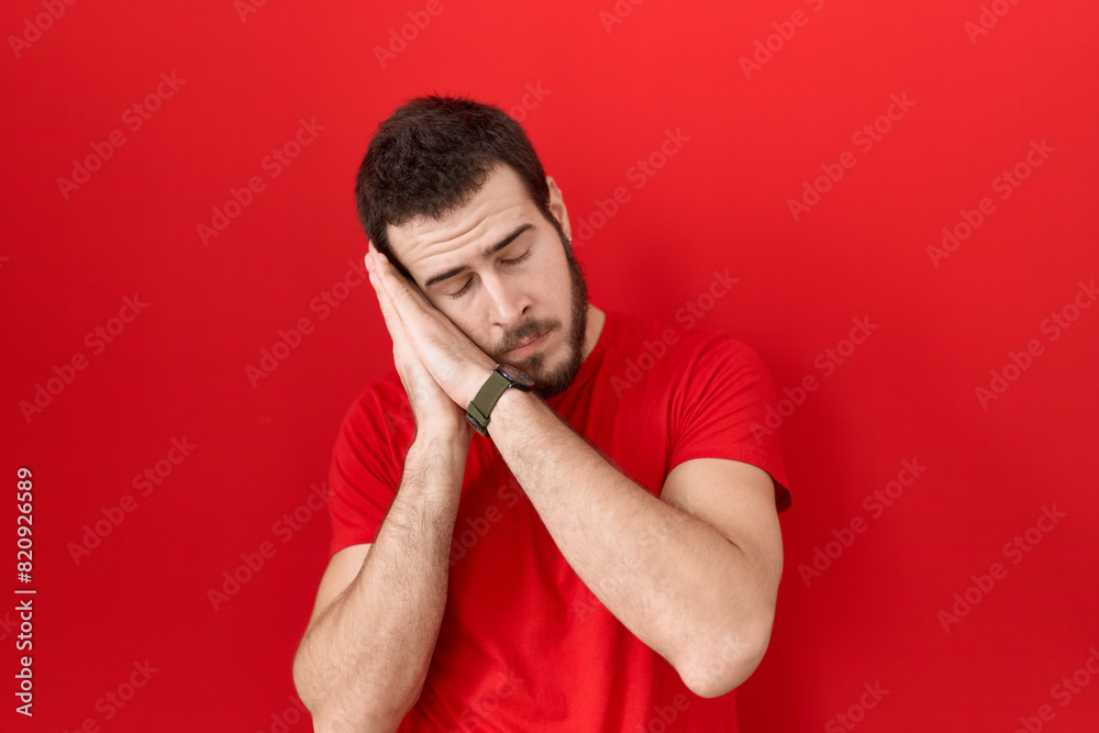 Young hispanic man wearing casual red t shirt sleeping tired dreaming and posing with hands together while smiling with closed eyes. Young hispanic man wearing casual red t shirt sleeping tired dreaming and posing with hands together while smiling with closed eyes.