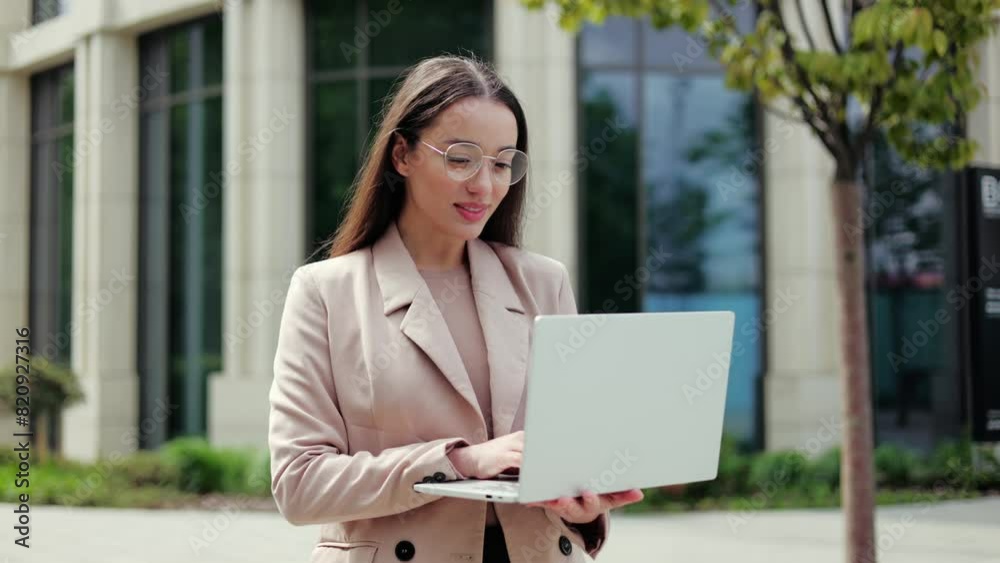 Joyful caucasian lady holding and opening modern laptop while standing in middle of square with beautiful building on background. Competent brunette female starting work process on fresh air. Joyful caucasian lady holding and opening modern laptop while standing in middle of square with beautiful building on background. Competent brunette female starting work process on fresh air.