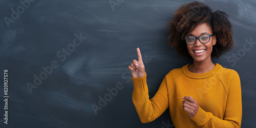 Person wearing a yellow sweater, gesturing with hand, denim jeans, in front of a blackboard background.