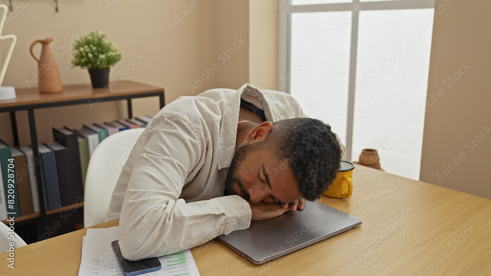A tired young man with a beard is sleeping on his laptop in a modern apartment's living room A tired young man with a beard is sleeping on his laptop in a modern apartment's living room