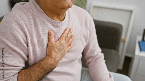 A senior man clutching his chest in a living room, portraying potential health issues. photo