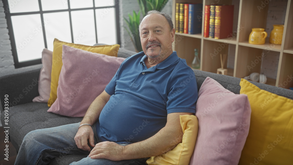 Relaxed mature man with a moustache sitting comfortably in a colorful, modern home's living room on a grey couch. Relaxed mature man with a moustache sitting comfortably in a colorful, modern home's living room on a grey couch.