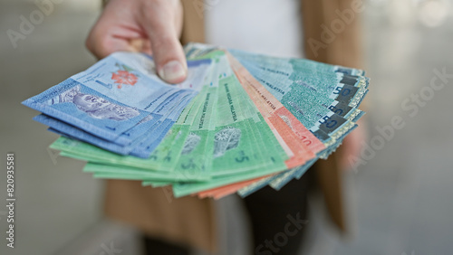 Close-up of a male hand holding malaysian ringgit currency on an urban street backdrop.