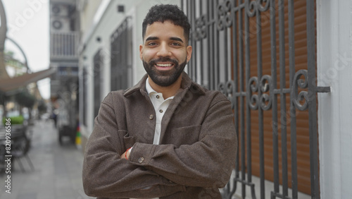 Smiling young hispanic man with beard standing arms crossed on urban city street photo