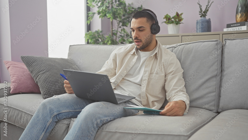 Hispanic man working on laptop with headphones in a modern living room apartment