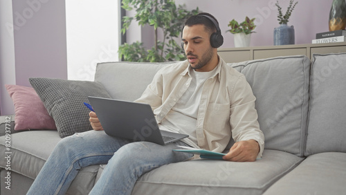 Hispanic man working on laptop with headphones in a modern living room apartment © Krakenimages.com