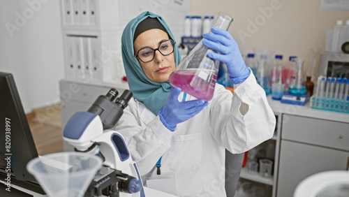 A woman scientist in a hijab examines a flask with pink liquid in a laboratory setting  suggesting healthcare research.
