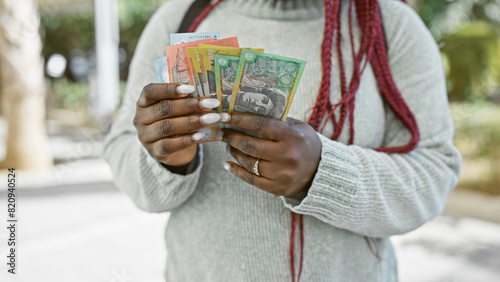 Australian currency held by a woman with braids outdoors in a lush park.