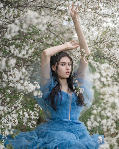A girl in a blue dress is sitting under a cherry blossom