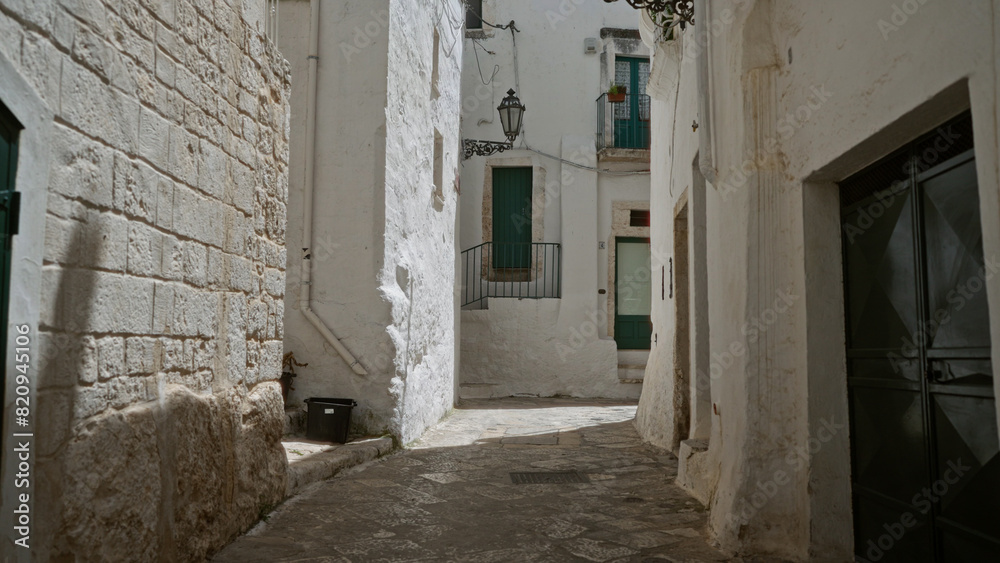 A quaint alleyway with whitewashed stone buildings, green doors, and wrought iron railings in ostuni, puglia, italy, europe.
