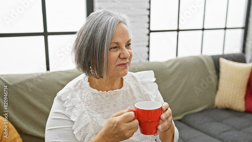 Schilderij op canvas Mature woman holding coffee mug sitting in living room on couch
