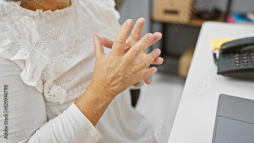 Mature woman experiencing hand pain at her office desk, perhaps from arthritis or overuse.