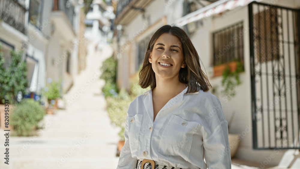 Fototapeta premium Young beautiful hispanic woman standing smiling at typical spanish old town