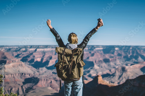 Back view of young wanderlust feeling victory conquering mountain in Grand Canyon, female traveler with backpack raising hands enjoying beautiful nature from high rocky hills getting to destination photo